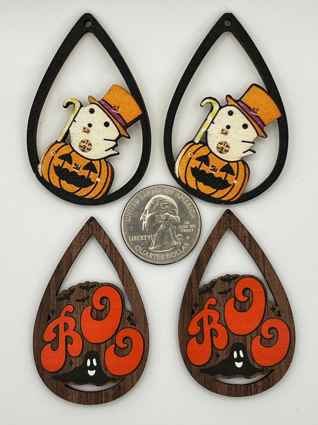 Four teardrop-shaped wood pendants with ghost and 'Boo' designs next to a quarter for scale.