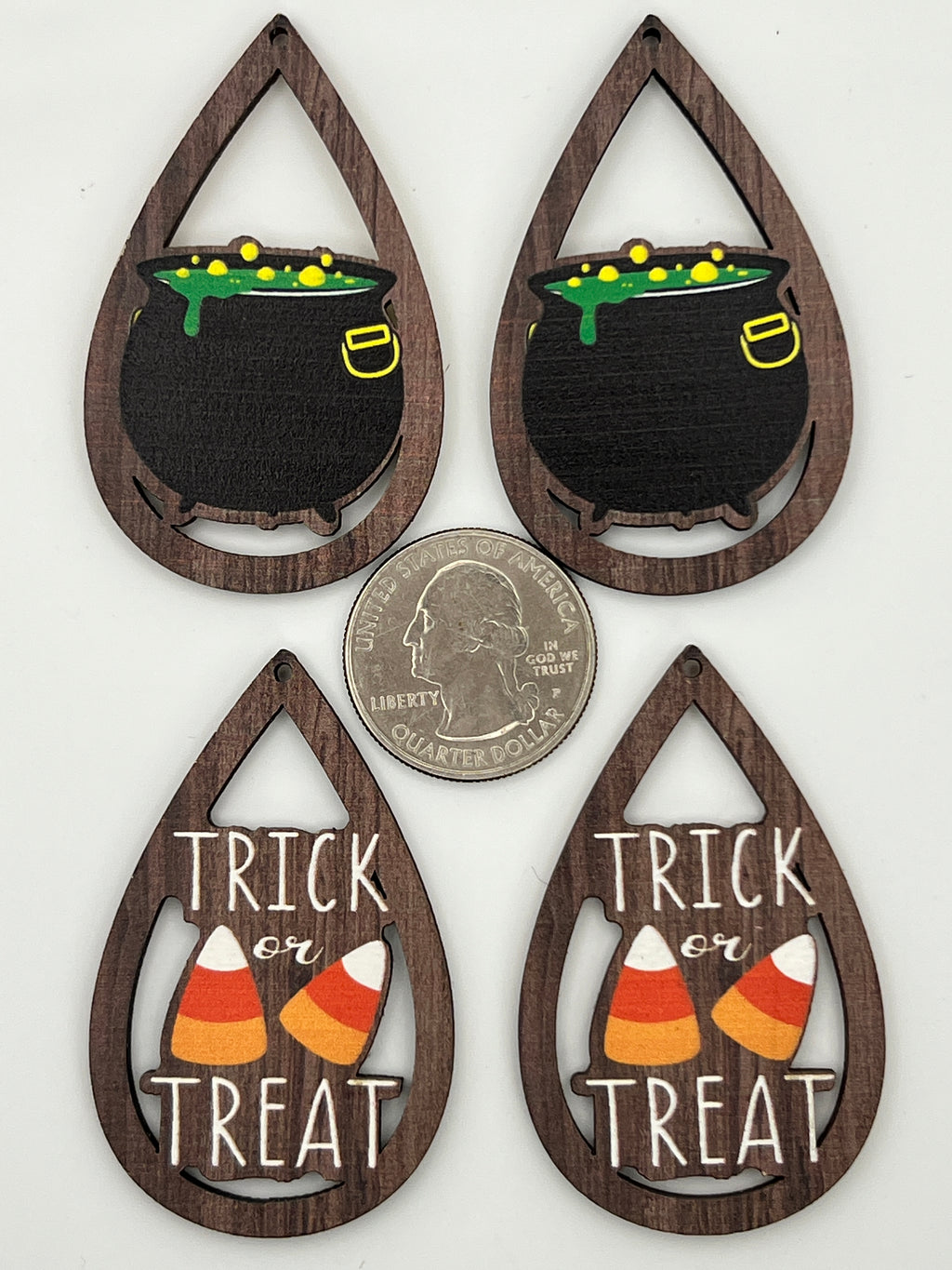 Four teardrop wood pendants with Halloween cauldron and Trick or Treat designs next to a quarter.