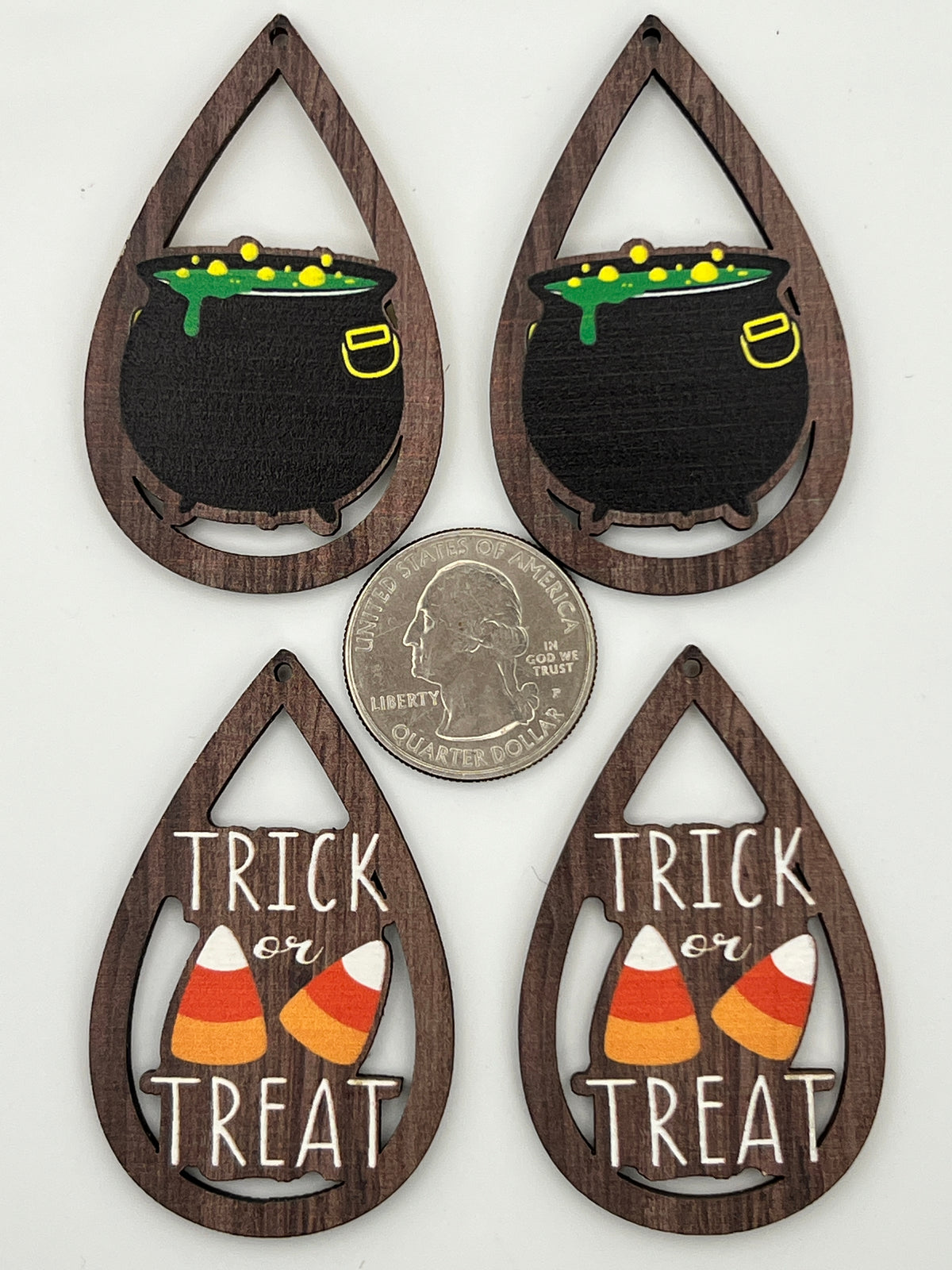 Four teardrop wood pendants with Halloween cauldron and Trick or Treat designs next to a quarter.