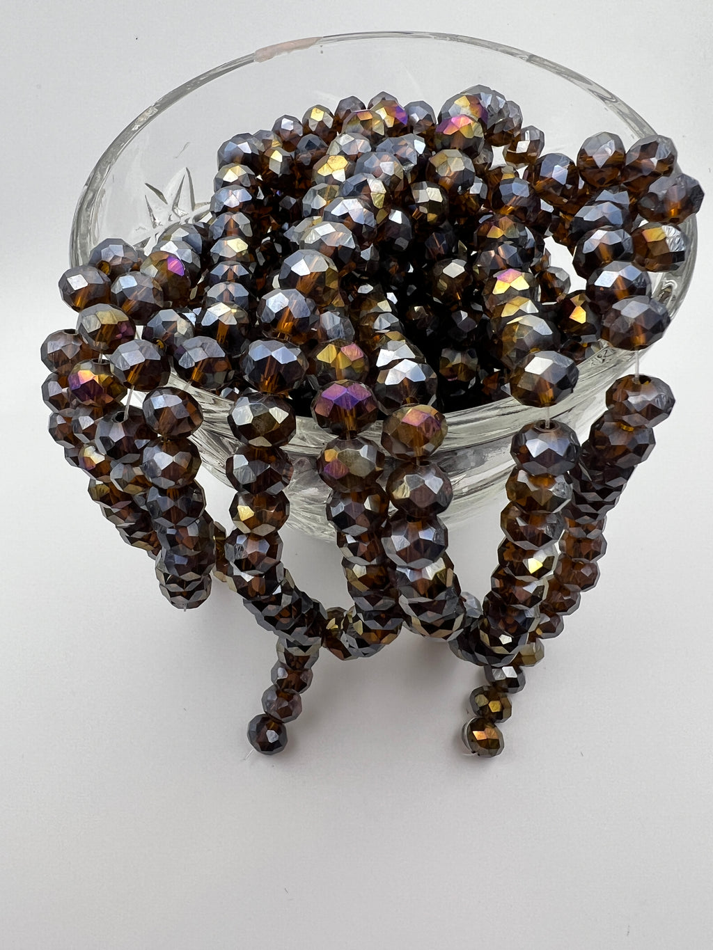 Strands of faceted 8x6mm saddle brown AB electroplated glass rondelle beads in a clear glass bowl.