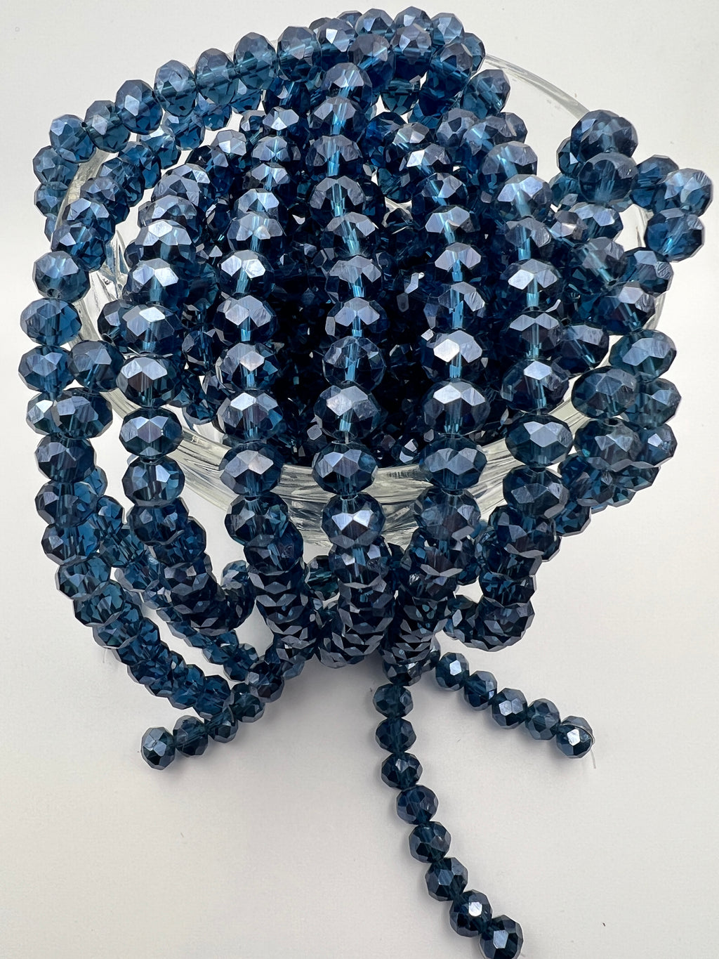 Strands of faceted 8x6mm marine blue glass rondelle beads with a pearl luster finish in a glass bowl