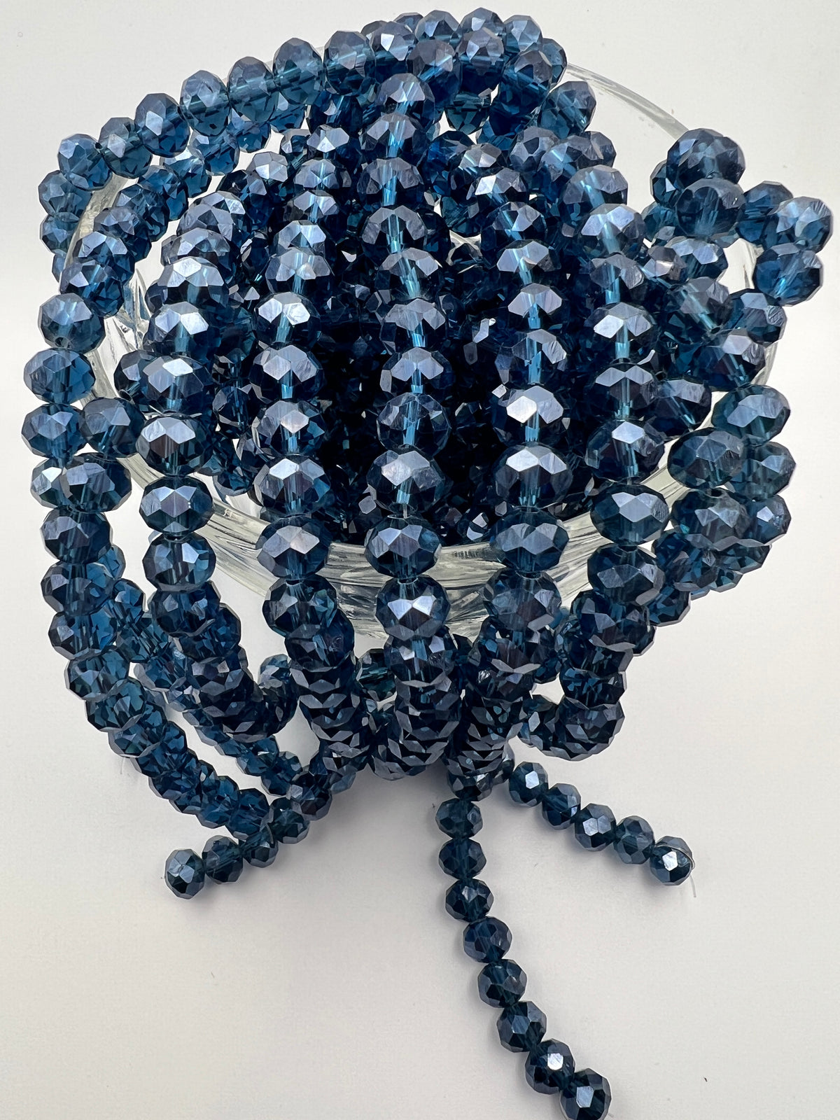 Strands of faceted 8x6mm marine blue glass rondelle beads with a pearl luster finish in a glass bowl