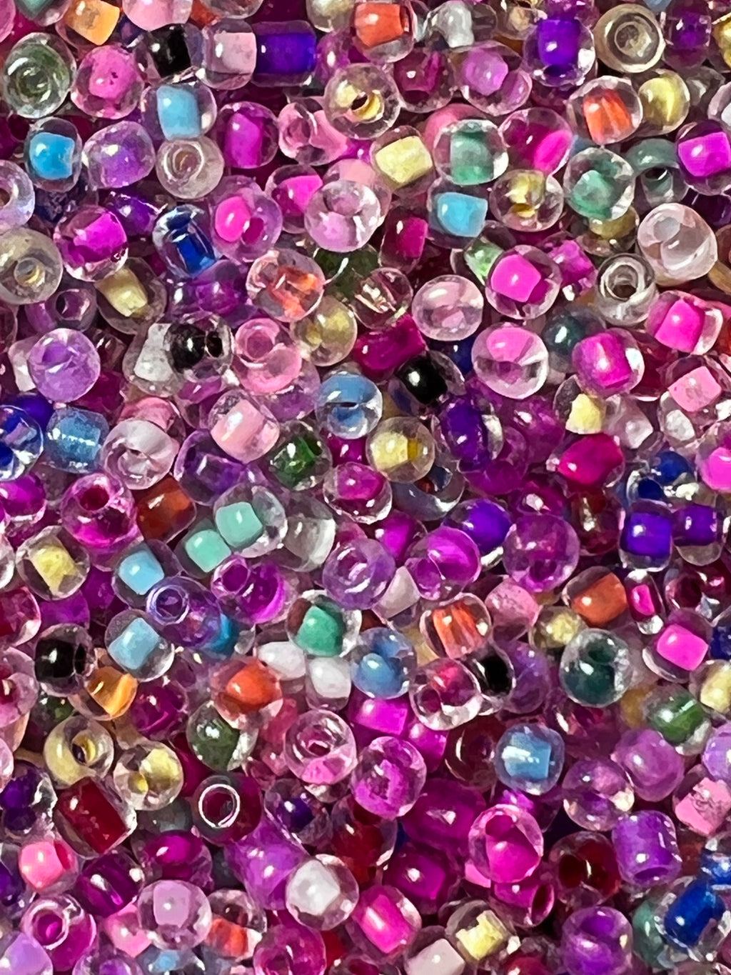 Close-up of mixed 8/0 glass seed beads with inside color in shades of purple, pink, blue, and orange.