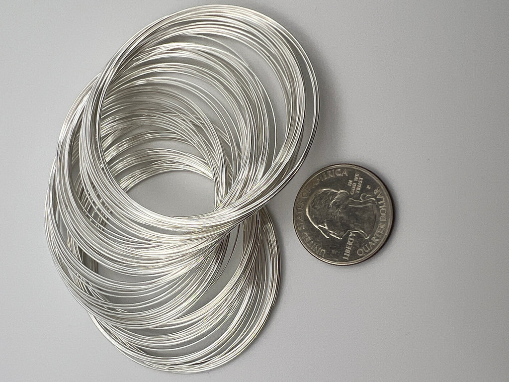 100 loops of silver carbon steel memory wire for bracelets next to a US quarter for scale.