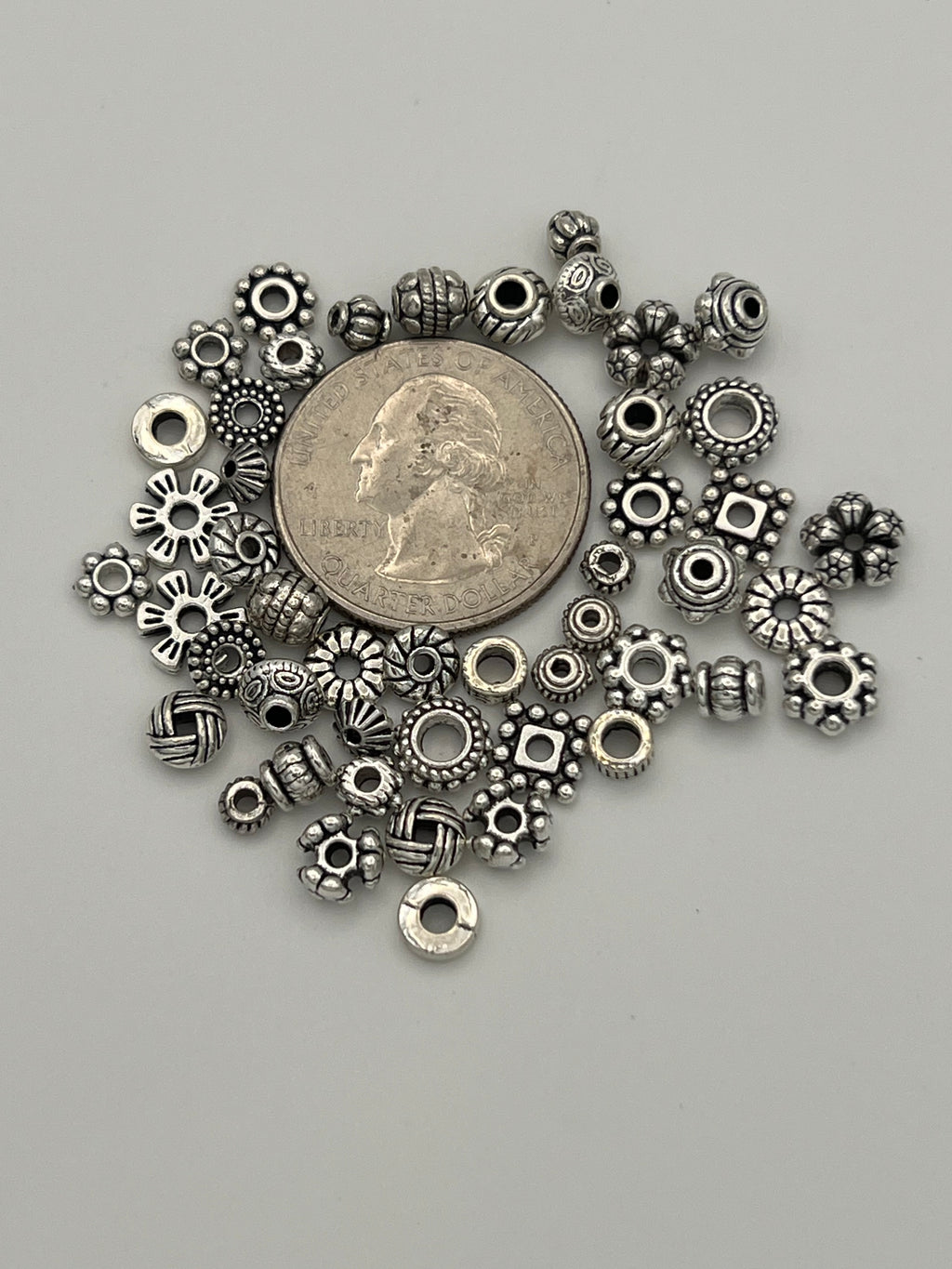50 mixed Tibetan style spacer beads in various shapes and sizes around a quarter.
