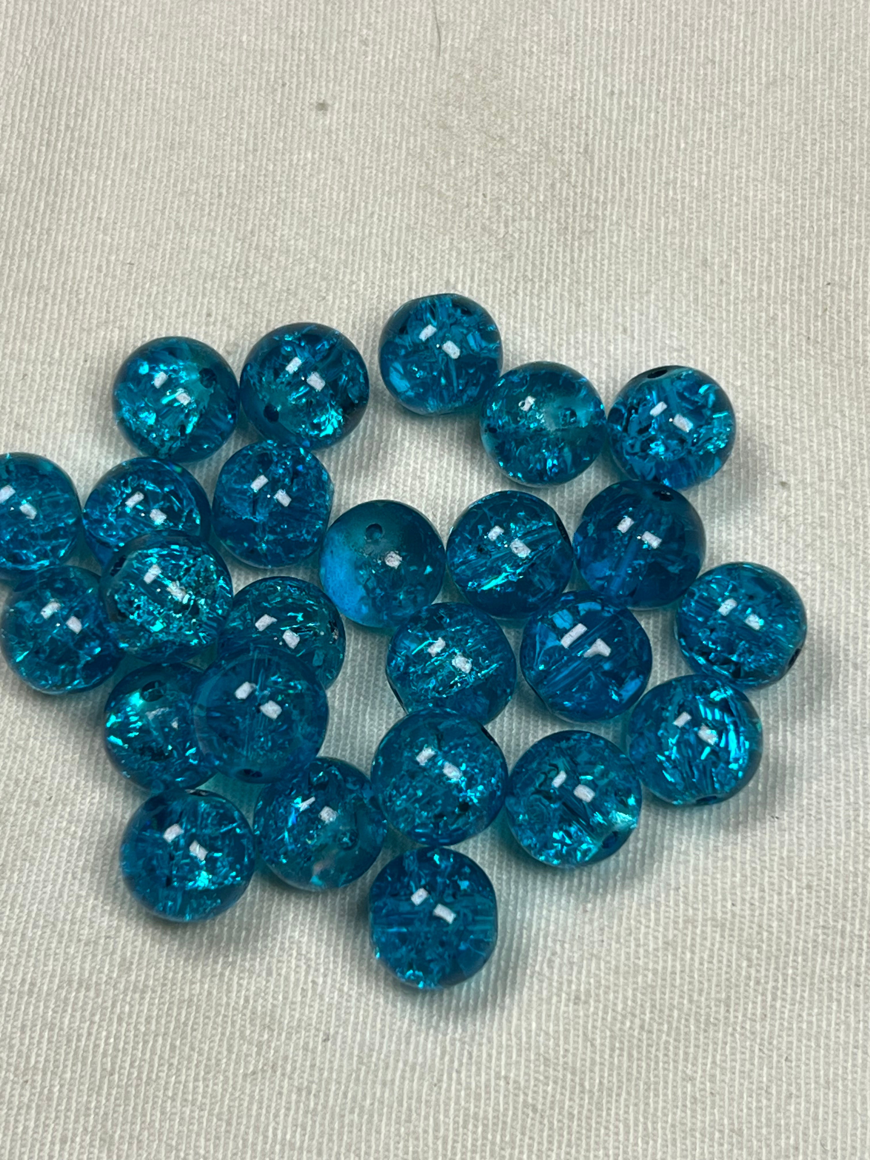 35 10mm turquoise crackle glass beads scattered on a white textured surface.